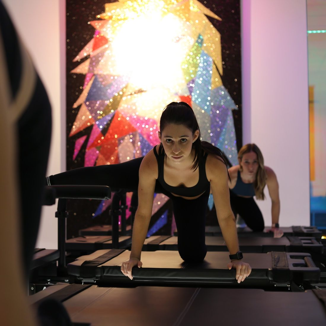 Student in a kneeling leg lift in front of the APEX mural